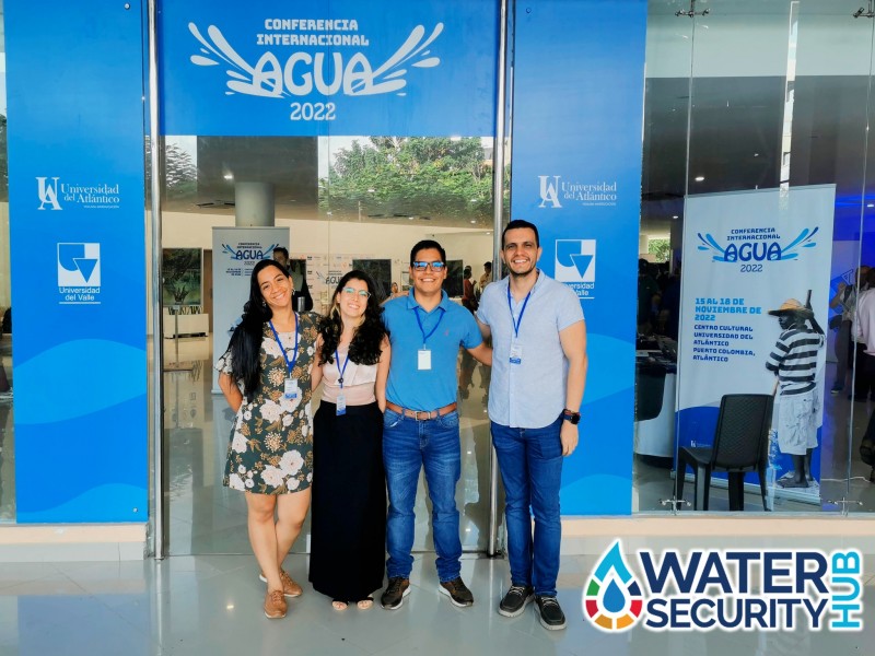 Four members of the team stand together smiling in front of the entrance to the AGUA Conference